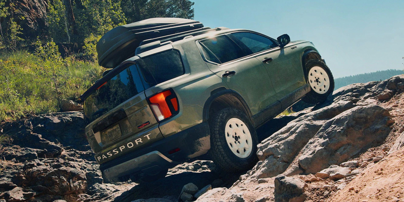 A green Honda Passport SUV navigating over rocky terrain with a roof cargo box.