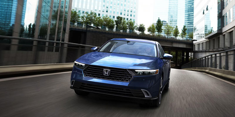 A blue Honda sedan driving through a cityscape with tall buildings.