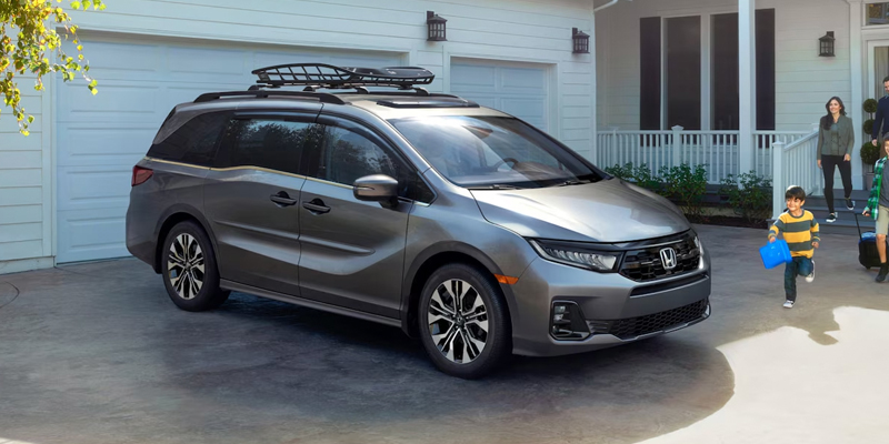 A gray Honda minivan parked in a driveway with a family walking towards it.