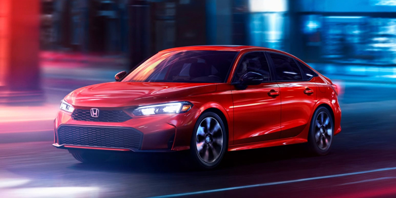 Red Honda sedan driving through a city street at night with motion blur.