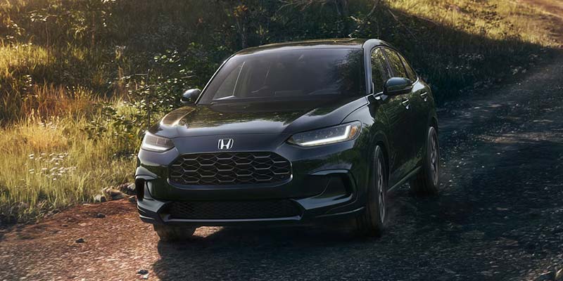 Black Honda SUV driving on a dirt road surrounded by grass and trees.