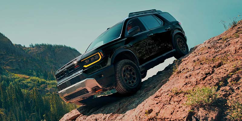 Black SUV climbing a rocky off-road trail in a mountainous landscape.