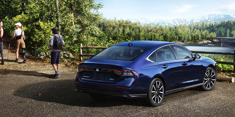 A 2026 Honda Accord Sedan parked on a road, with hikers visible in the background enjoying the outdoors.